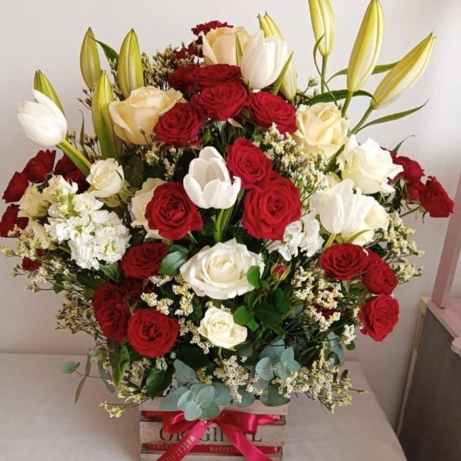 A vibrant flower arrangement in a rustic wooden crate featuring tulips, lilies, roses, and eucalyptus – handcrafted by MuscatFnC.